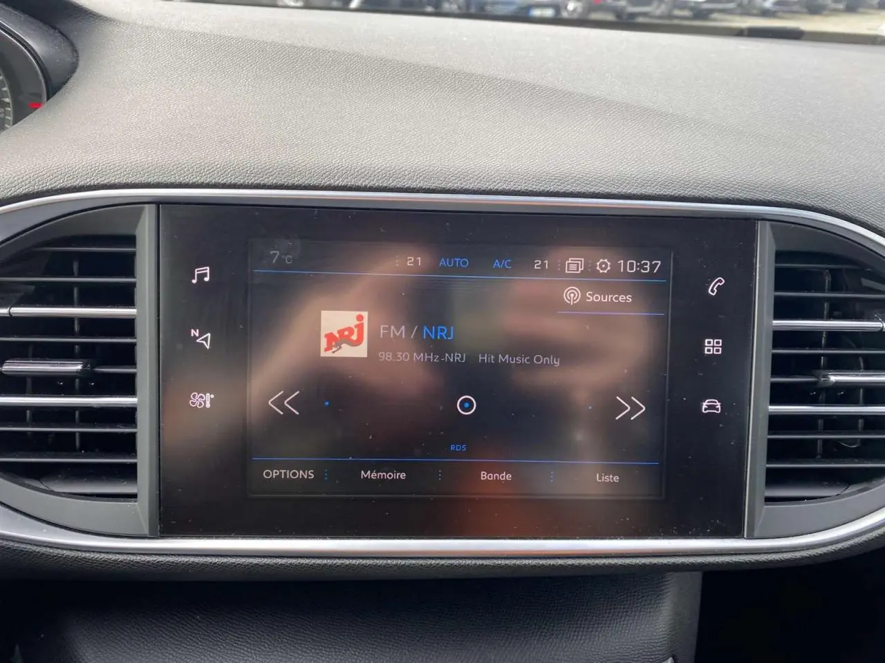 Écran tactile central du tableau de bord de la Peugeot 308 2018 affichant la radio FM NRJ, entouré de grilles d'aération noires.