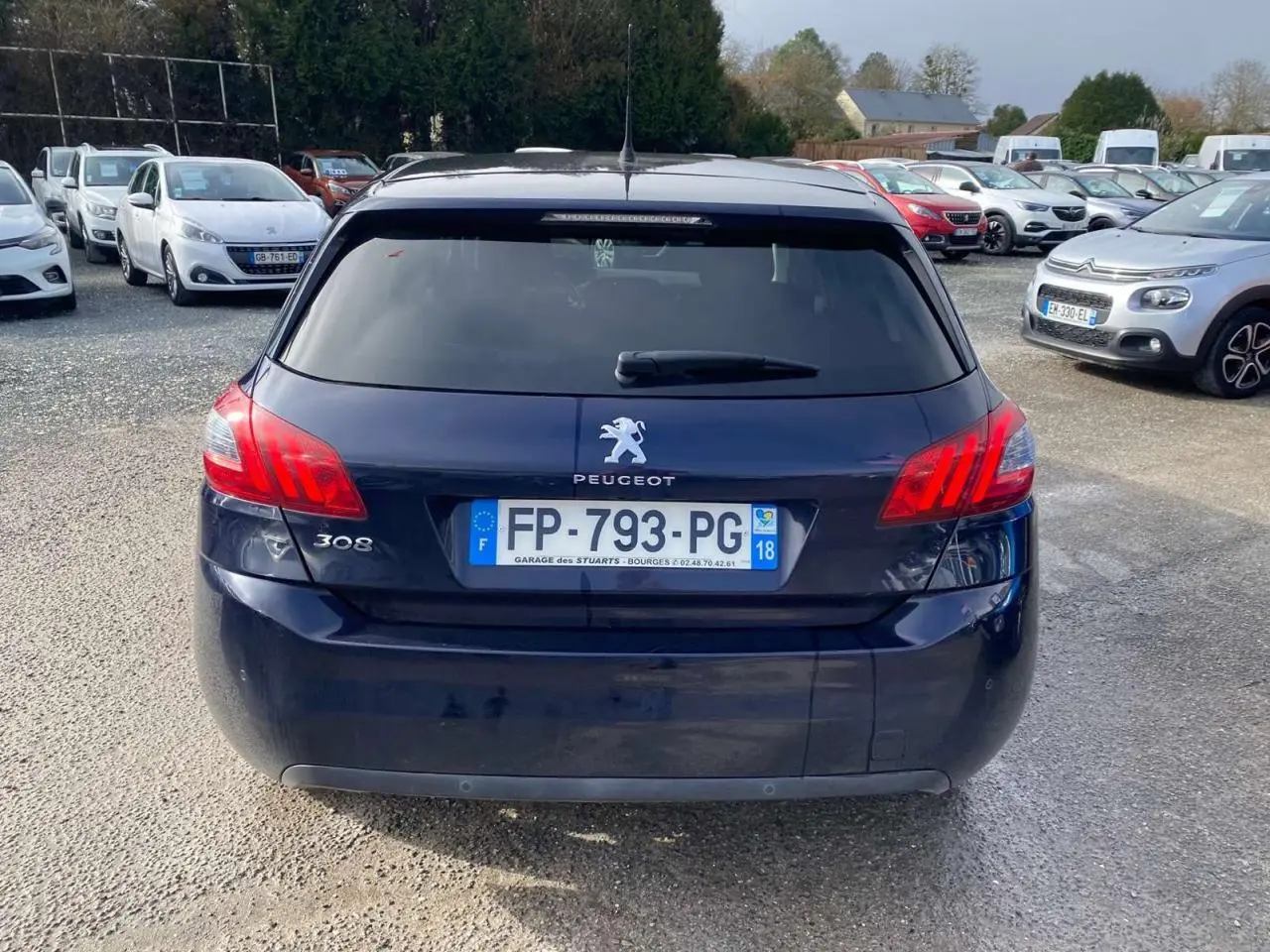 Vue arrière d'une Peugeot 308 bleu foncé avec feux arrière allumés et plaque d'immatriculation française visible.