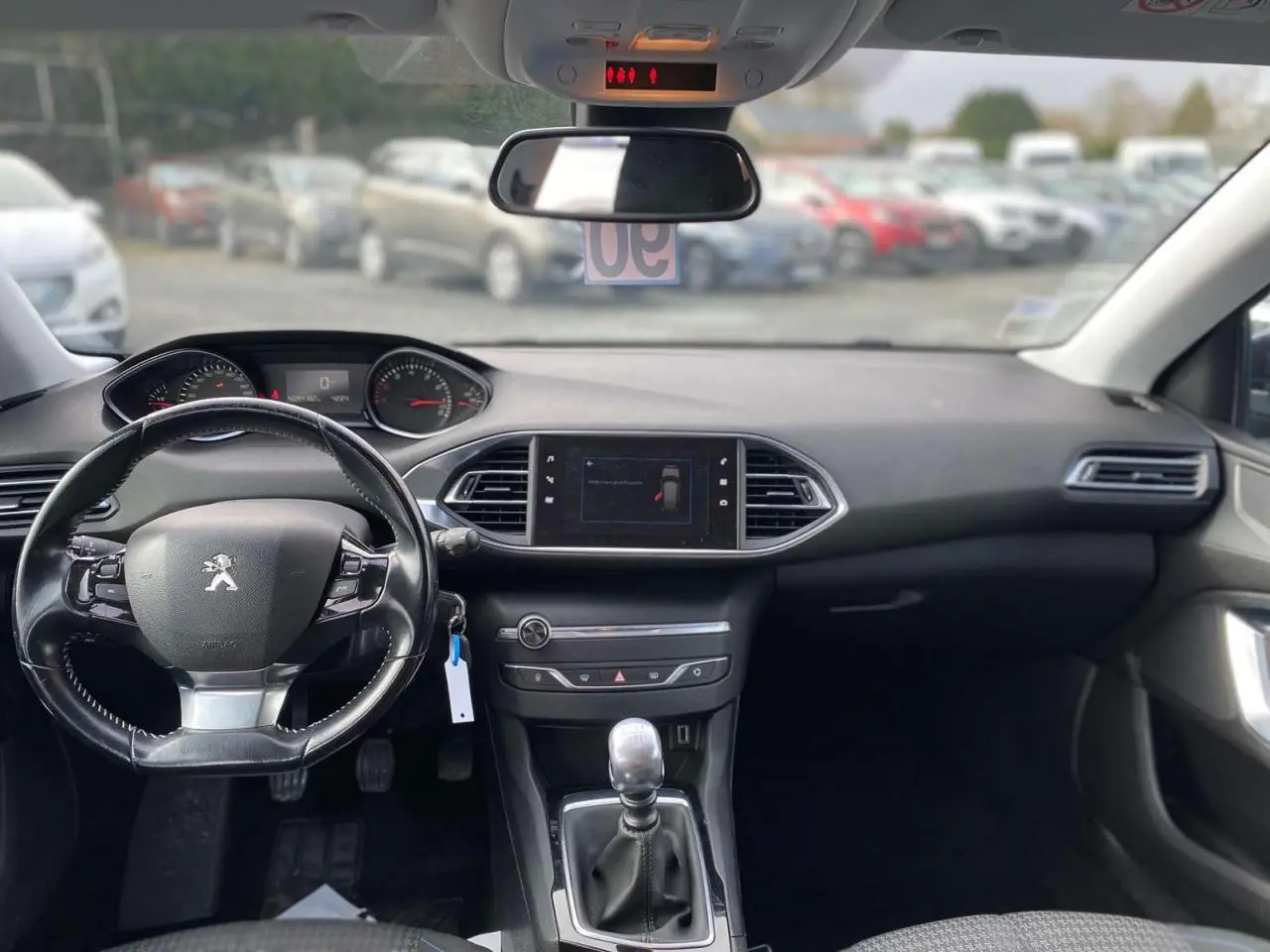 Vue intérieure avant du tableau de bord et volant noir d'une Peugeot 308 2018 avec boîte manuelle et écran central tactile.