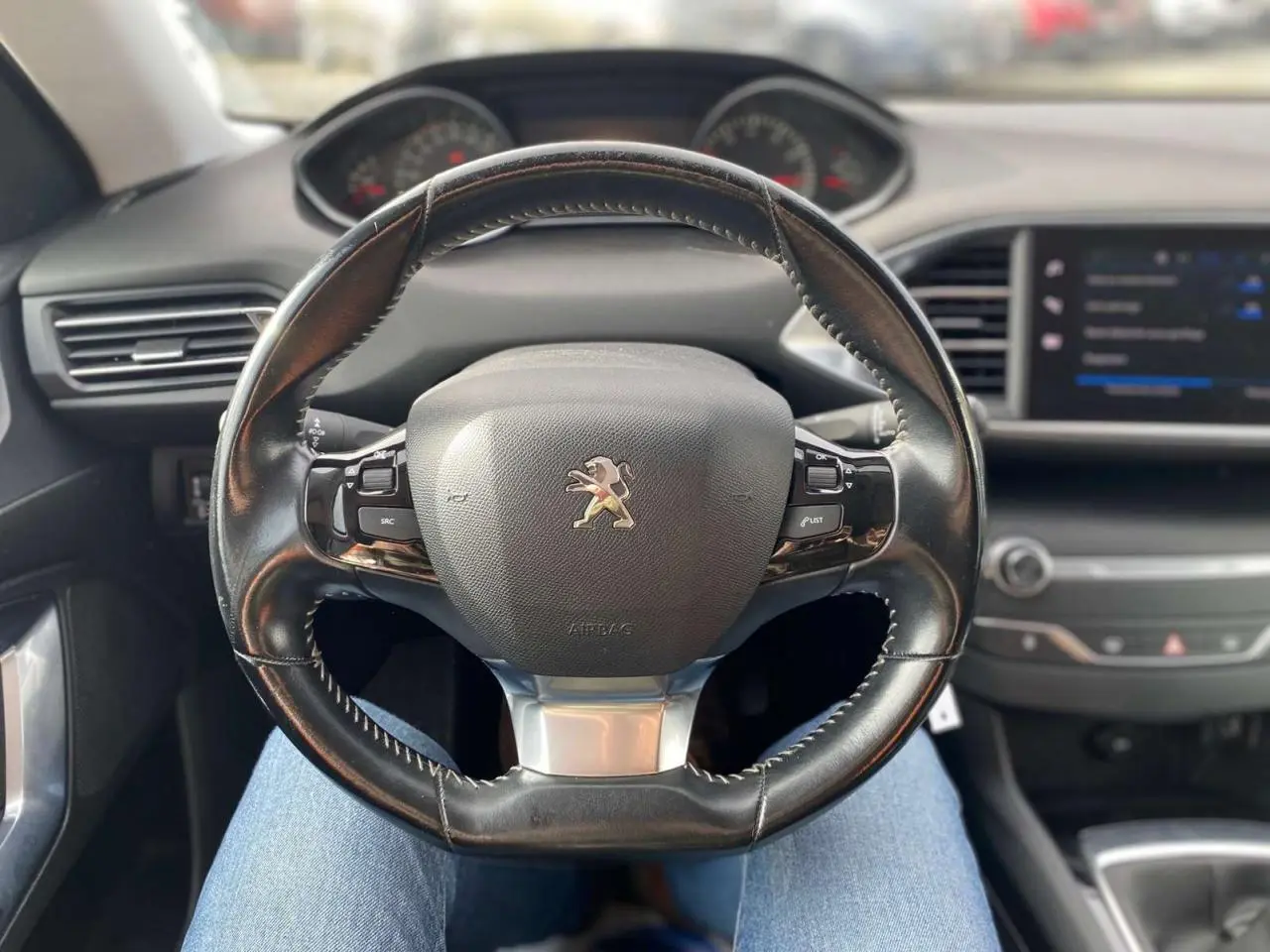 Volant en cuir noir avec logo Peugeot au centre, tableau de bord et écran tactile de la 308 style 2018 visible en arrière-plan