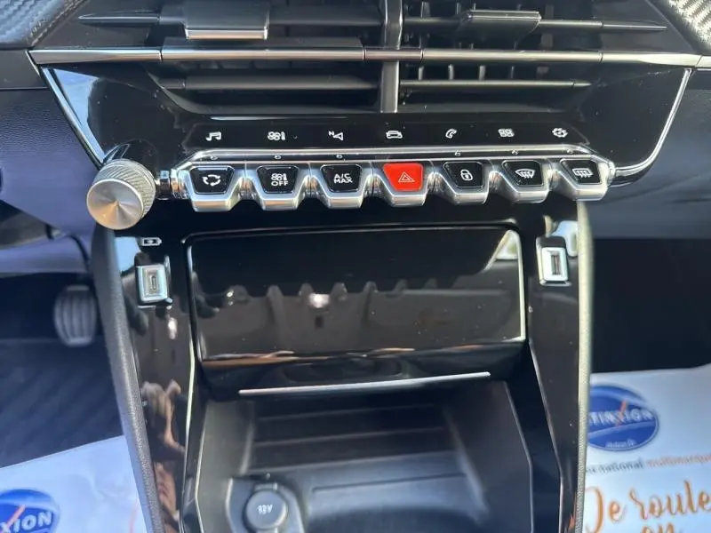 Gros plan sur la console centrale noire brillante du Peugeot 2008 2020, avec boutons de commande et molette argentée.