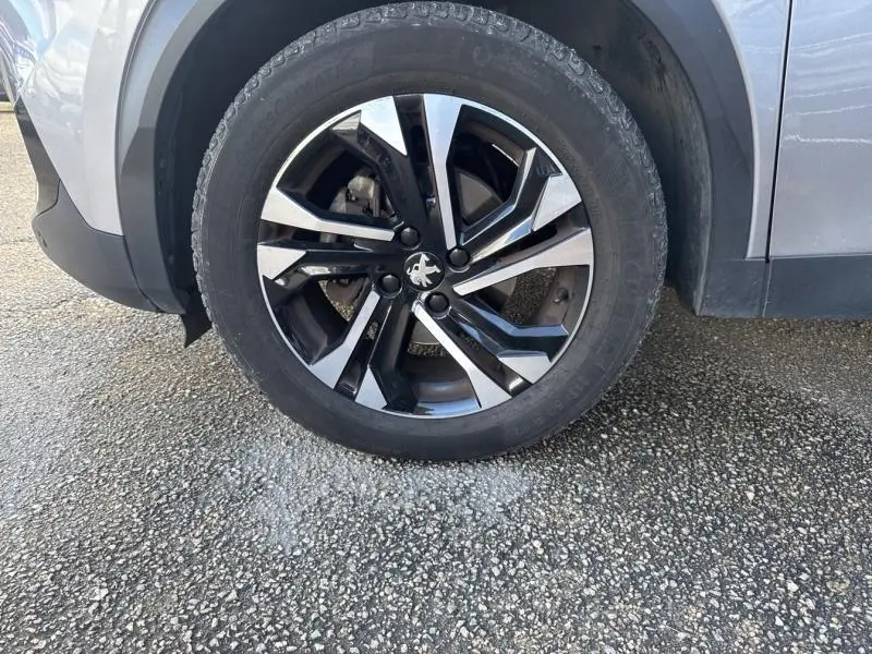 Gros plan sur la roue avant gauche d’un Peugeot 2008 gris Artense avec jante alliage bi-ton noire et argentée.