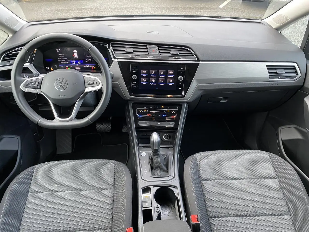 Vue intérieure frontale du tableau de bord et console centrale du Volkswagen Touran 2025 avec volant cuir multifonction et écran tactile.