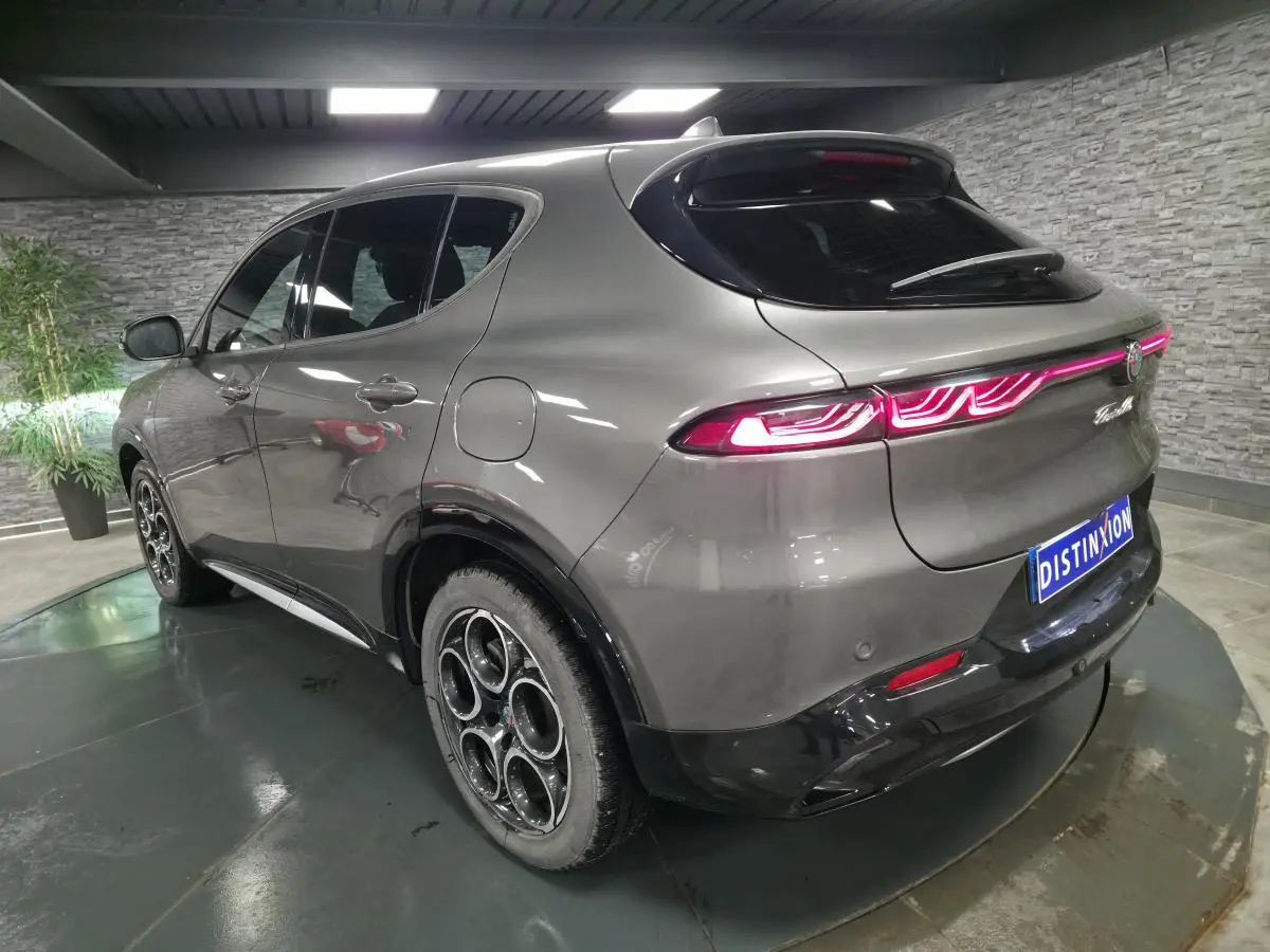Vue 3/4 arrière droite de l'Alfa Romeo Tonale gris métallisé avec feux arrière LED allumés en intérieur showroom.