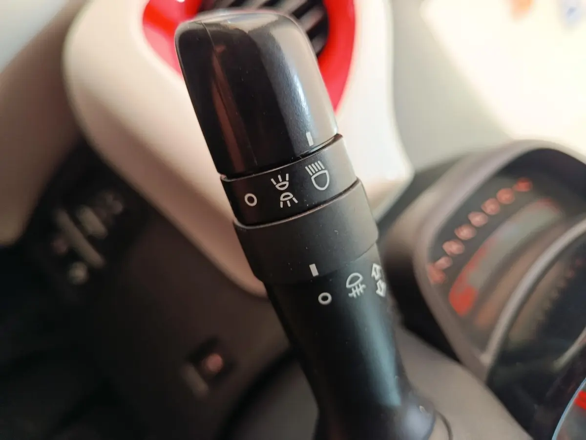 Gros plan sur la commande des phares dans l’habitacle blanc et rouge d’une Toyota Aygo 2016.
