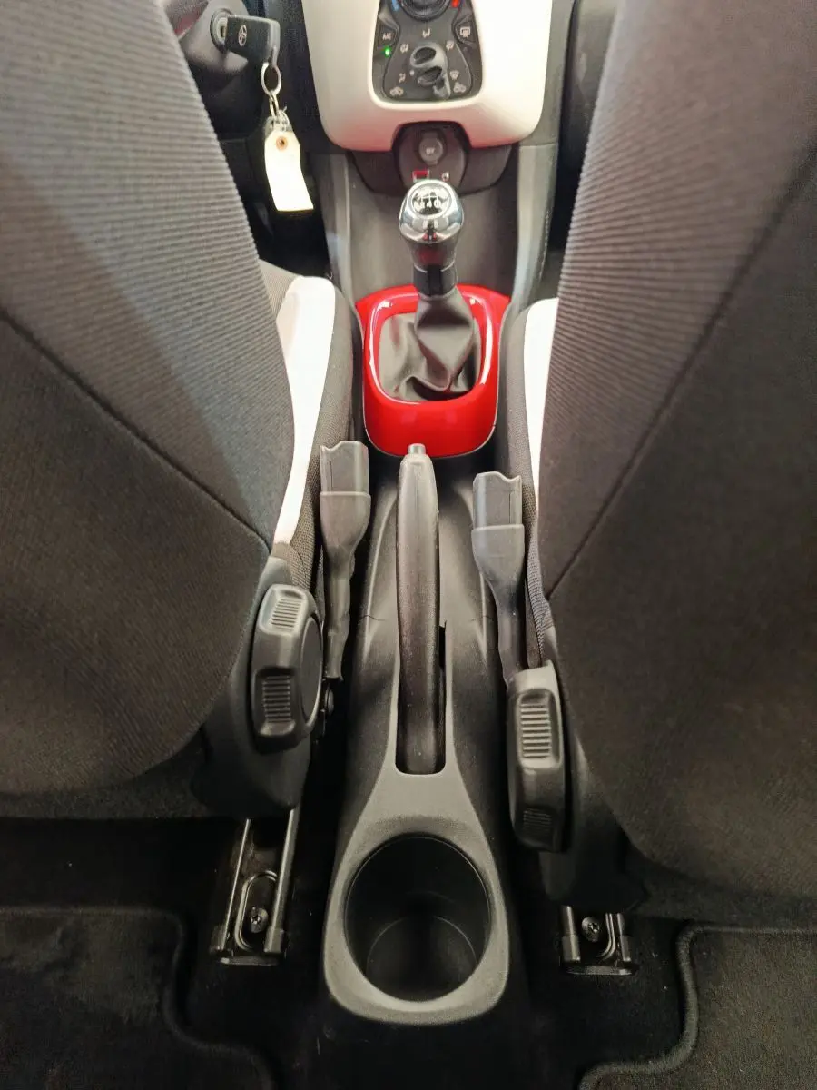 Vue intérieure centrée sur la console centrale d'une Toyota Aygo blanche, avec levier de vitesse manuel entouré d'un cadre rouge.