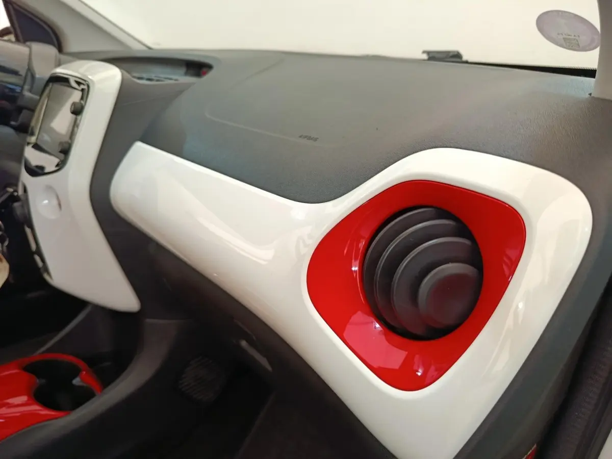 Détail intérieur du tableau de bord blanc et rouge de la Toyota Aygo 2016, avec aérateur rond rouge côté passager.