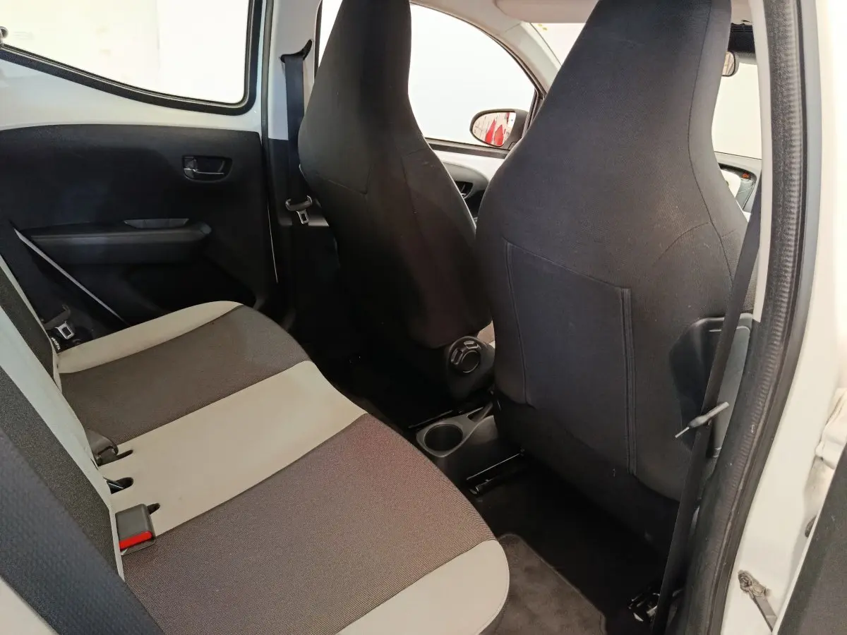 Vue intérieure arrière droite de la Toyota Aygo blanche, montrant la banquette bicolore et les dossiers des sièges avant noirs.
