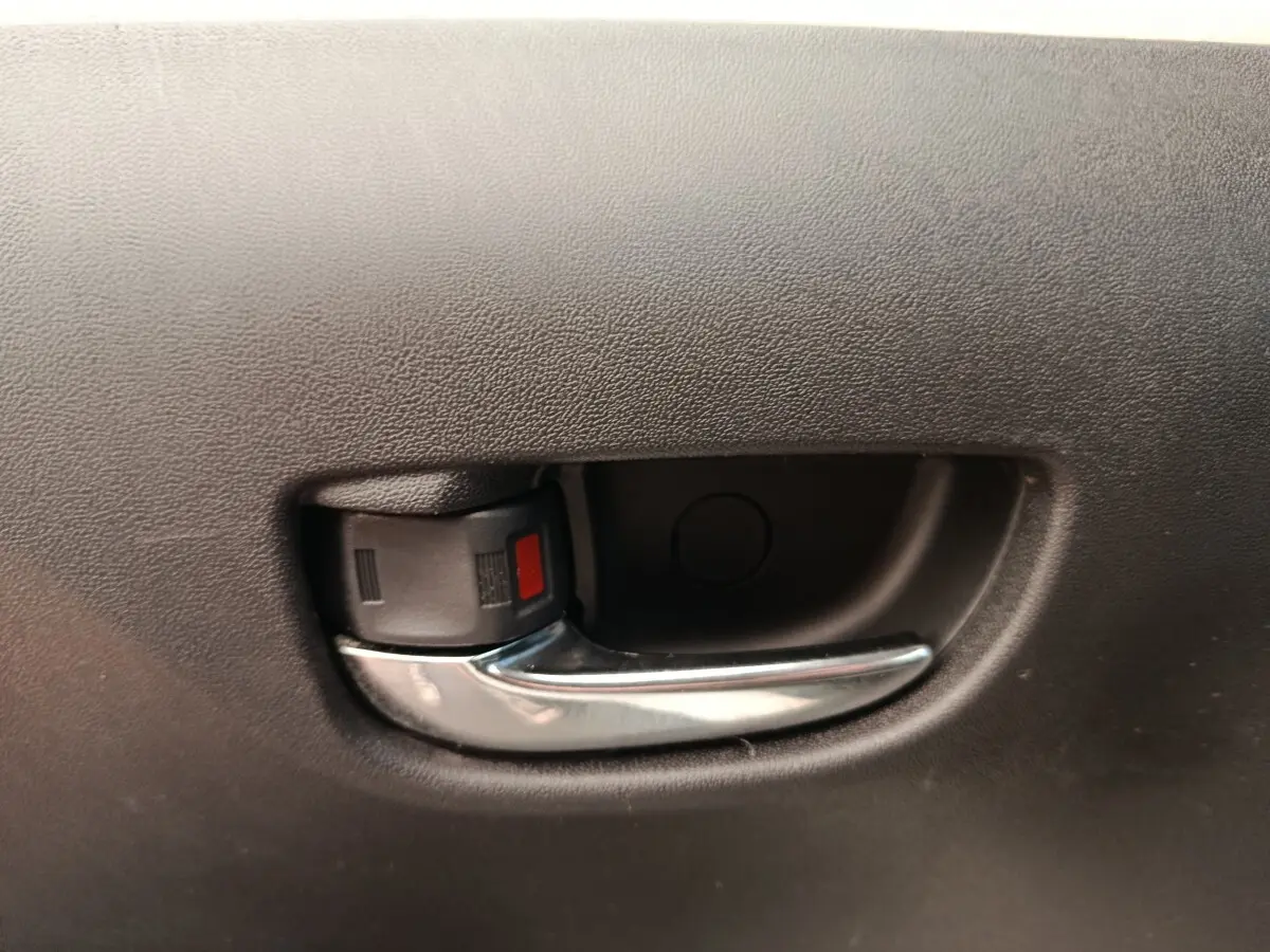Poignée intérieure de porte avant en plastique noir et chrome sur Toyota Aygo blanc, vue rapprochée.