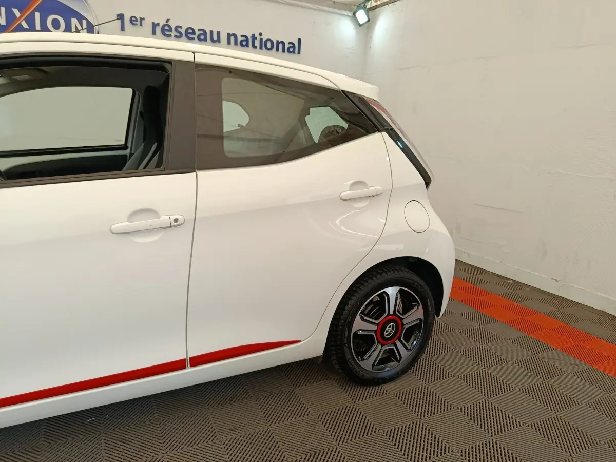 Vue côté droit arrière d'une Toyota Aygo blanche 2016 avec jantes noires et détails rouges sur la carrosserie.