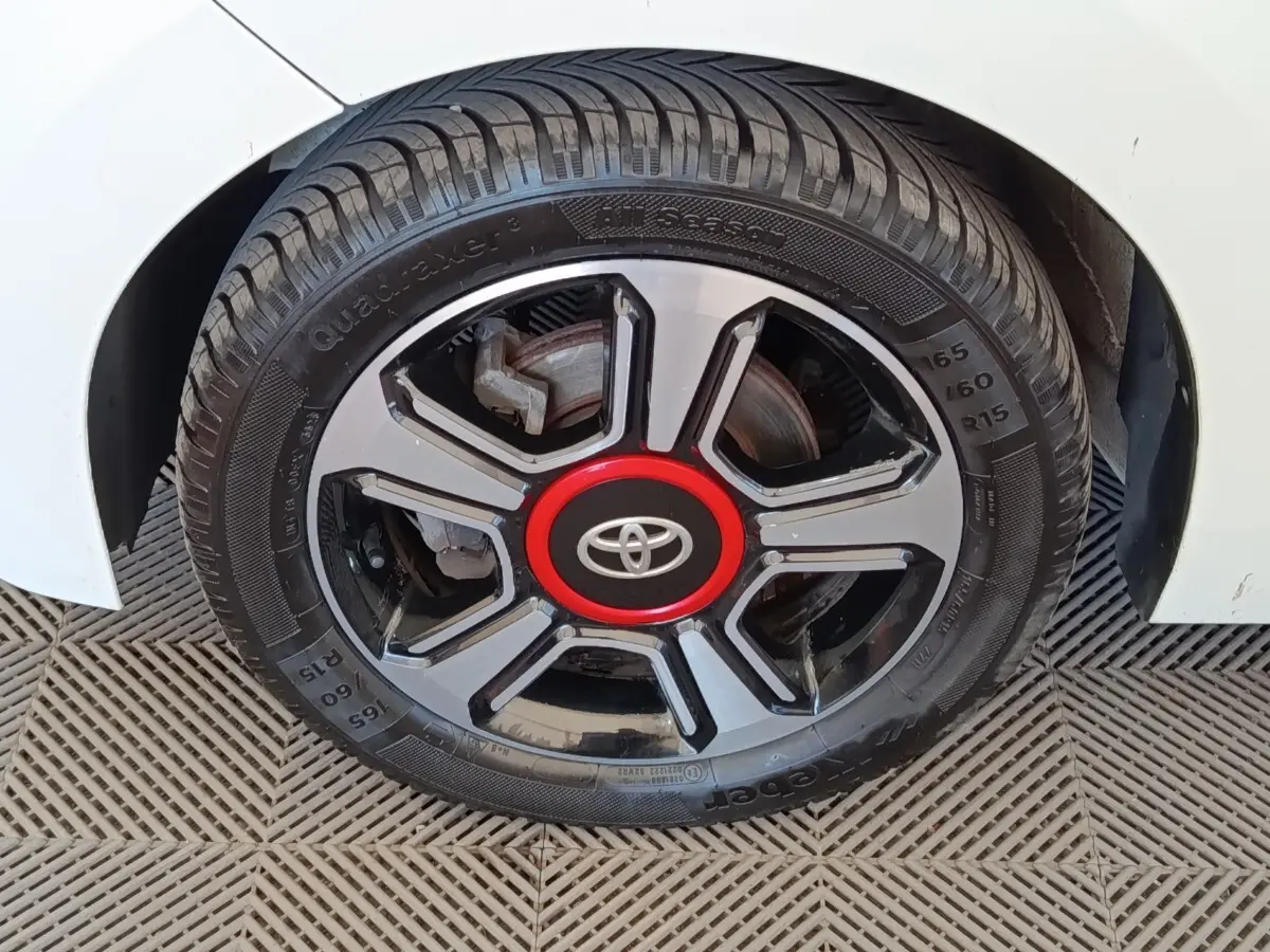 Gros plan sur la roue avant droite d'une Toyota Aygo blanche, avec jante noire et rouge au centre.