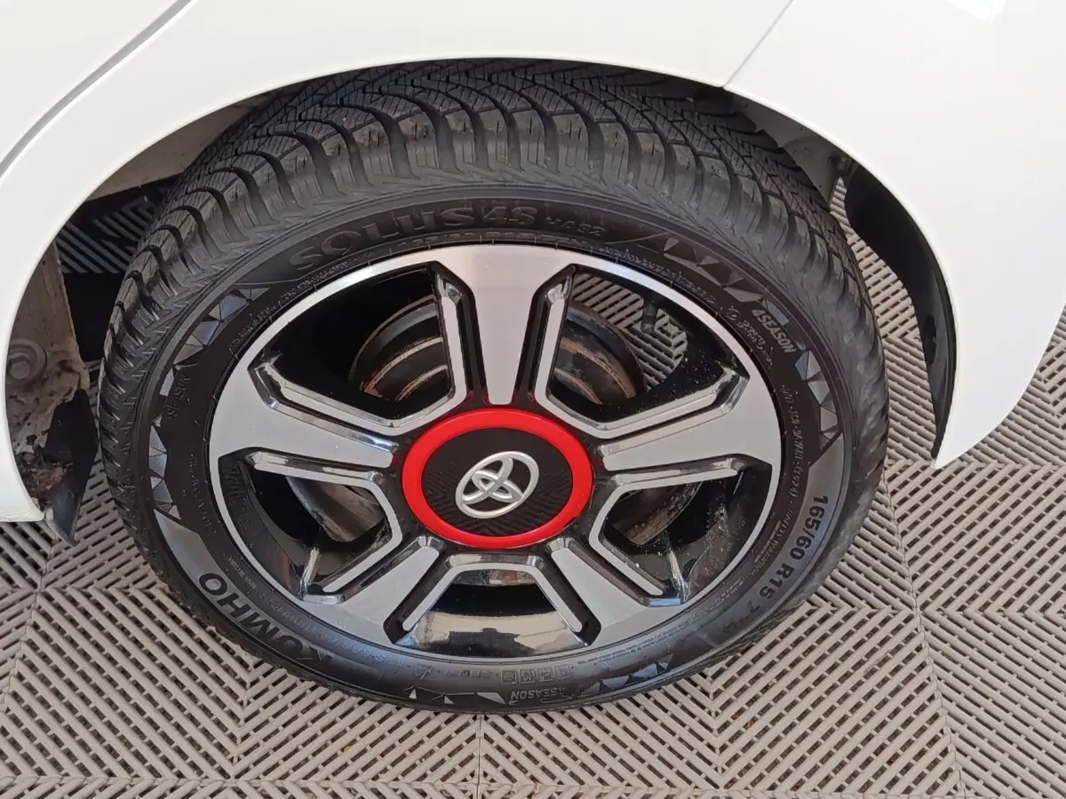 Gros plan sur la roue arrière droite d'une Toyota Aygo blanche avec jante noire et rouge distinctive.