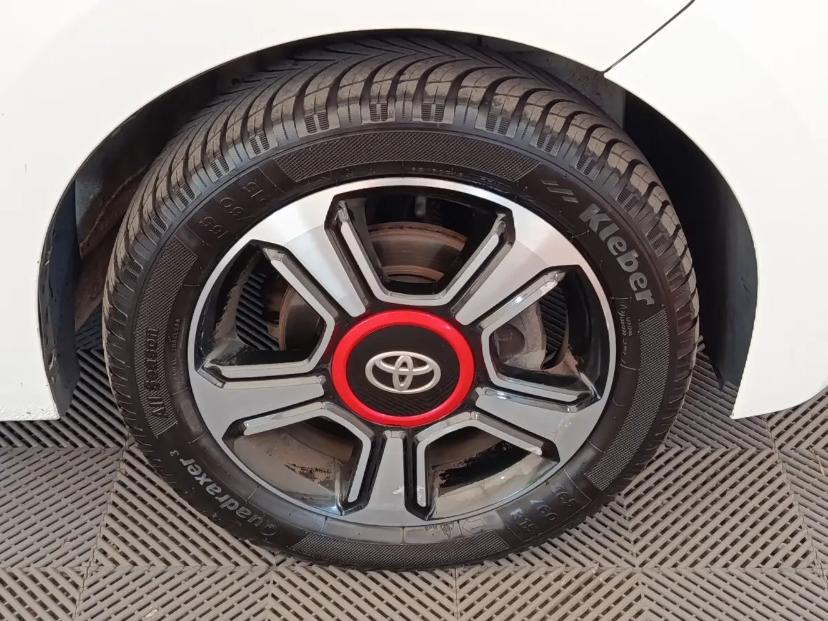 Gros plan sur la roue avant droite d'une Toyota Aygo blanche, jante noire et argent avec logo Toyota rouge au centre.