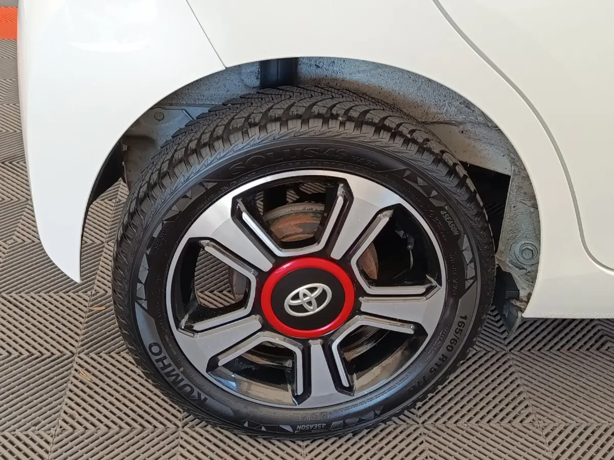 Gros plan sur la roue arrière droite blanche d’une Toyota Aygo 2016 avec jante noire et rouge distinctive.