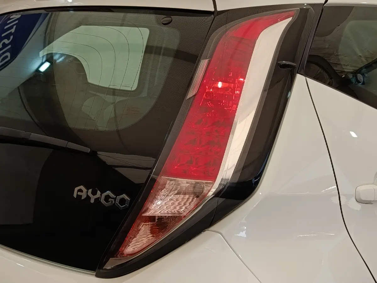 Gros plan sur l’arrière droit blanc d’une Toyota Aygo 2016, mettant en valeur le feu arrière et le logo AYGO.