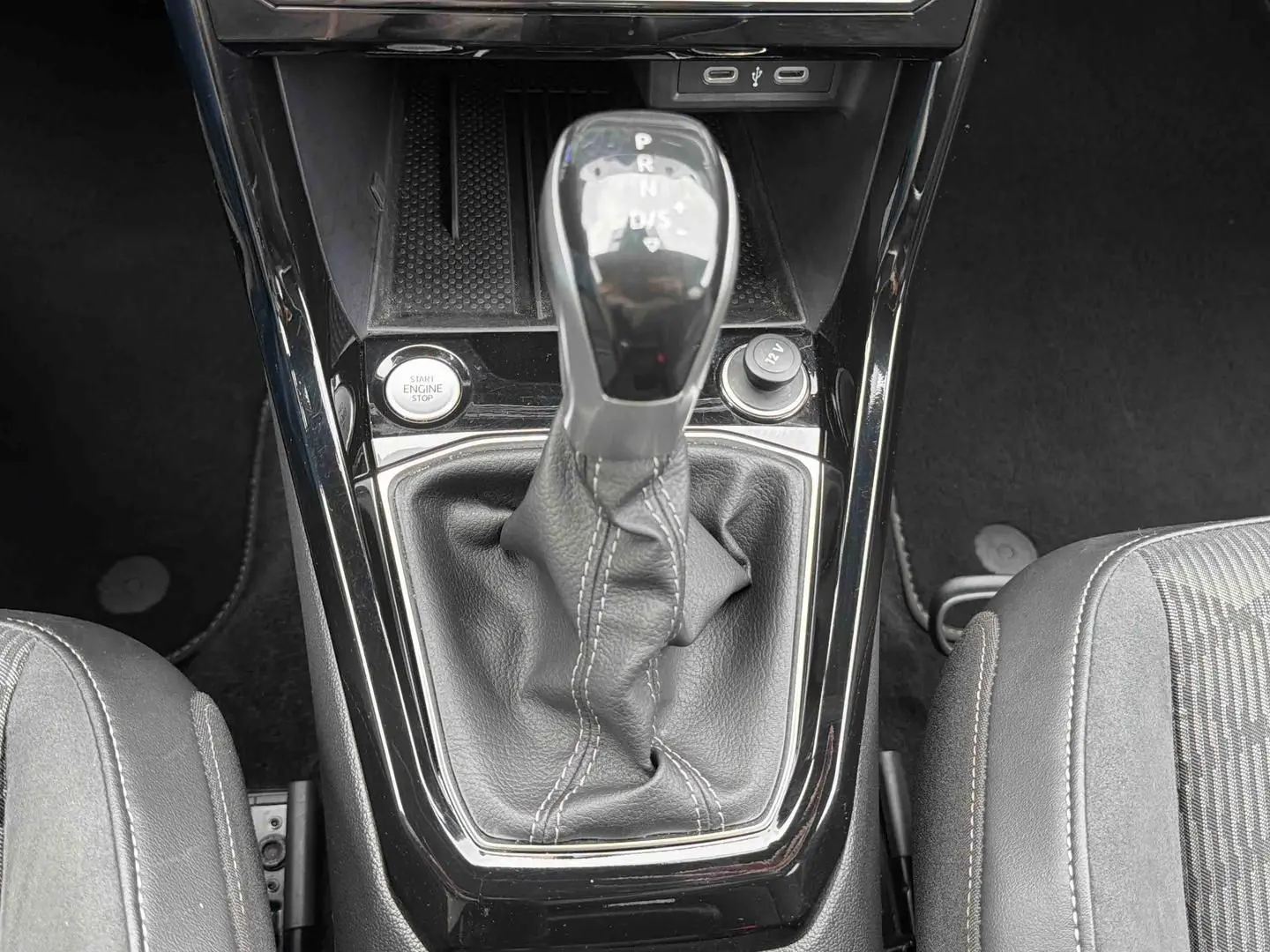 Gros plan sur la console centrale du Volkswagen T-Cross gris, mettant en valeur le levier de vitesse manuel et le bouton start/stop.