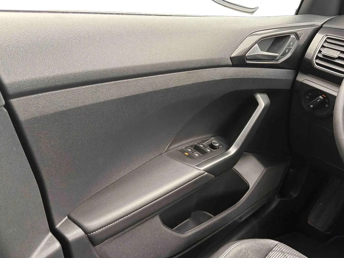 Vue intérieure côté conducteur du Volkswagen T-Cross gris, montrant la portière avec commandes des vitres et rétroviseurs.