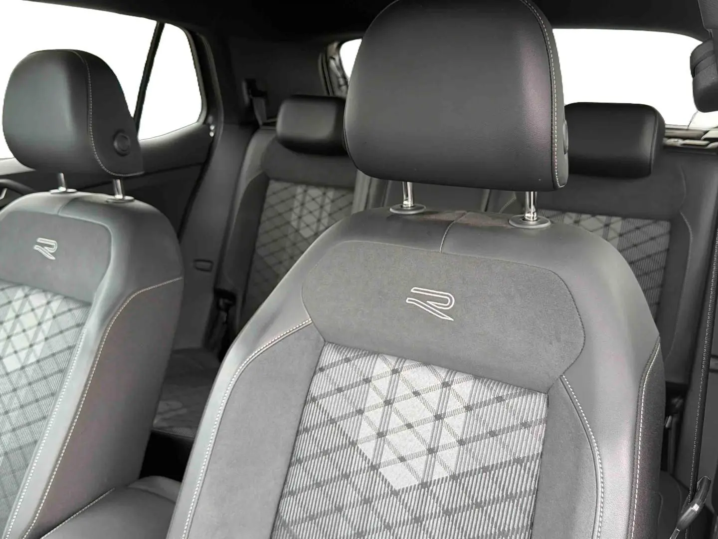 Gros plan sur les sièges avant gris du Volkswagen T-Cross avec surpiqûres blanches et logo R brodé.