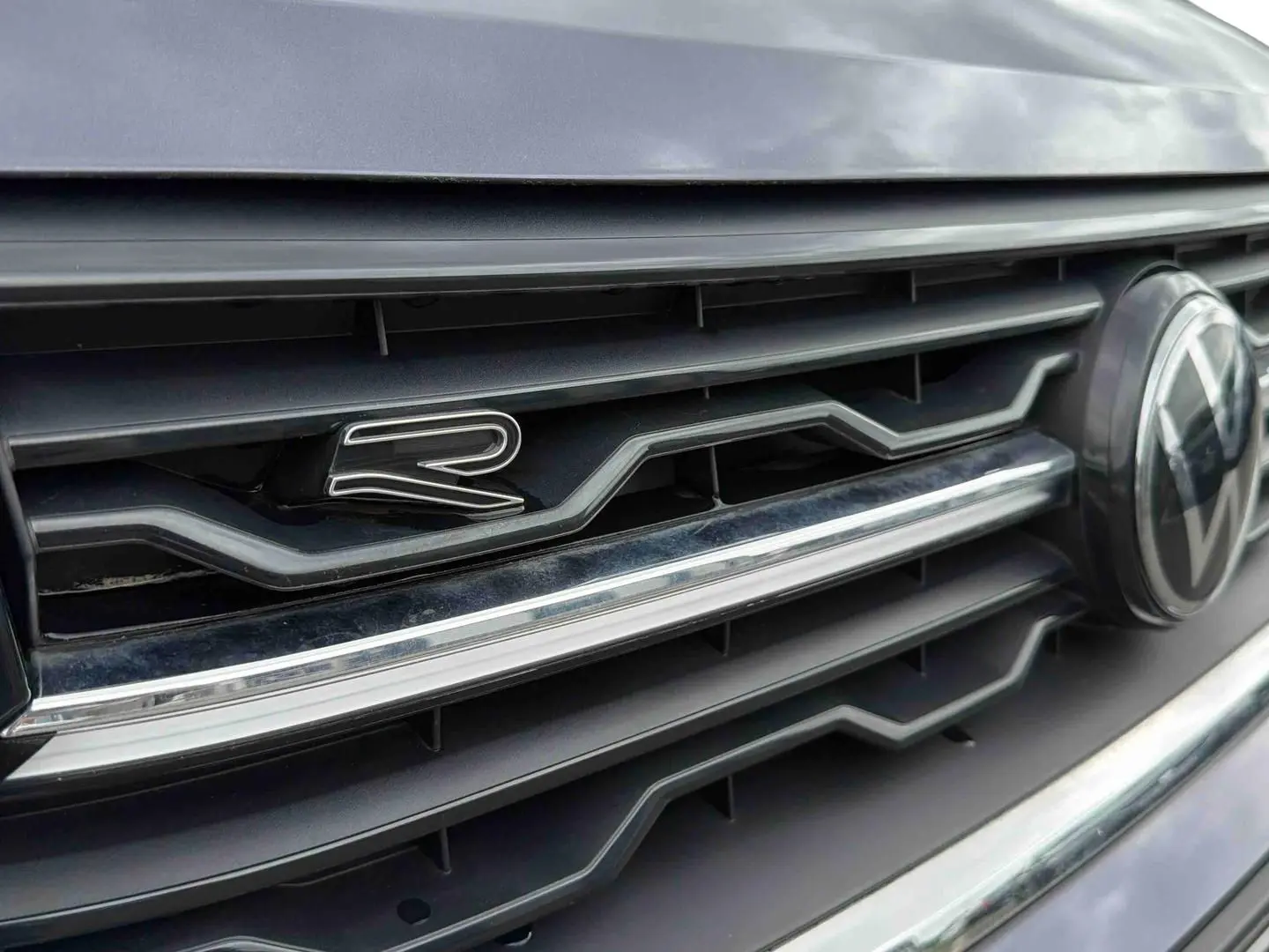 Gros plan sur la calandre grise du Volkswagen T-Cross avec logo VW et badge "R" distinctif.