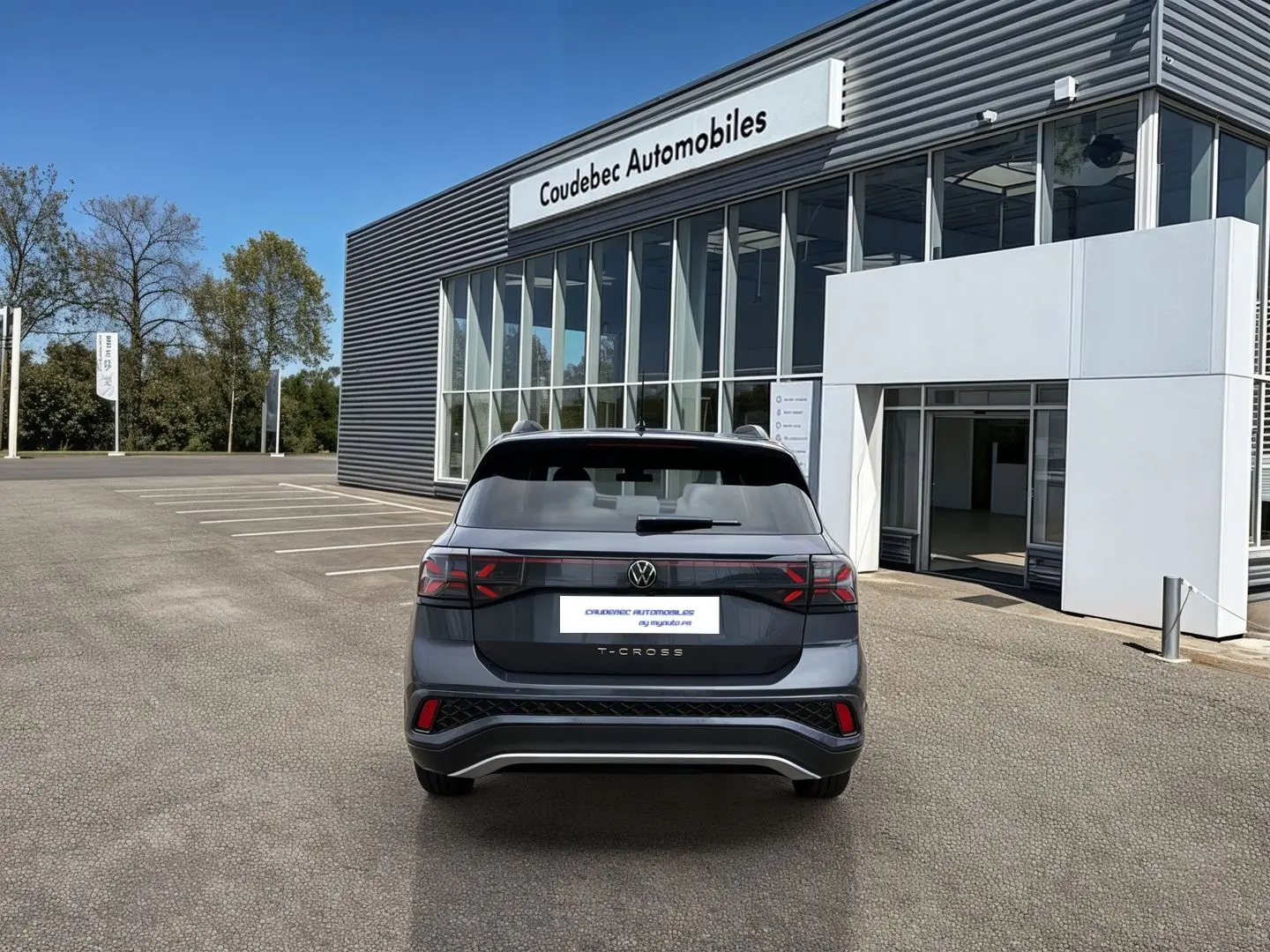 Vue arrière d'un Volkswagen T-Cross gris 2025 avec feux LED et pare-chocs R-Line devant un concessionnaire.