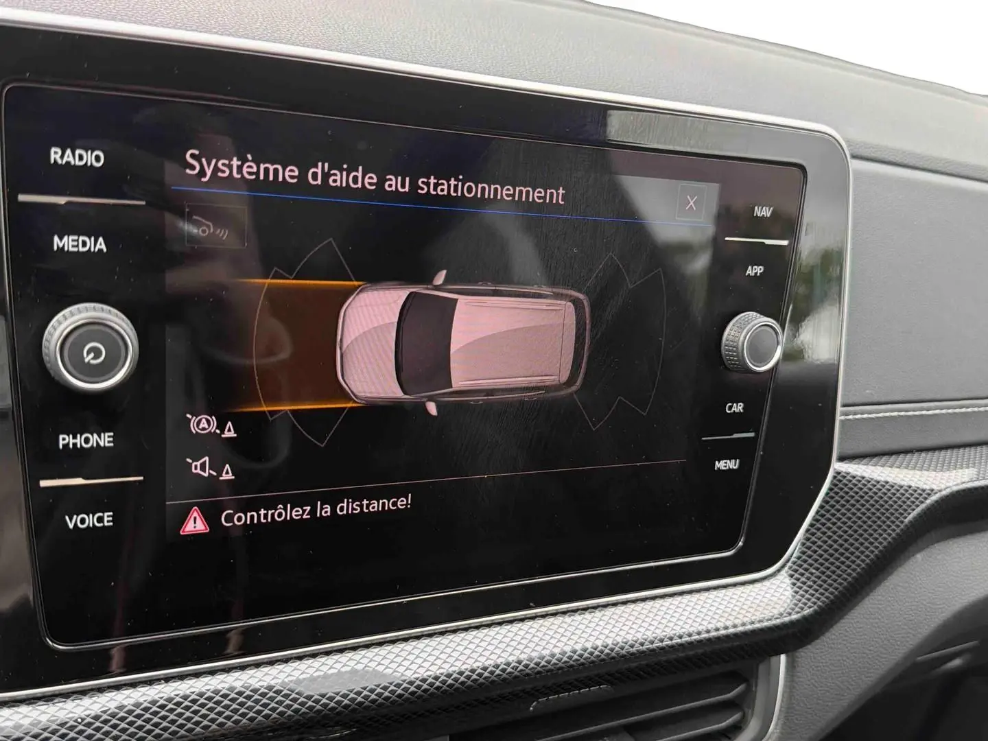 Écran tactile intérieur montrant le système d'aide au stationnement du Volkswagen T-Cross gris, vue rapprochée du tableau de bord.