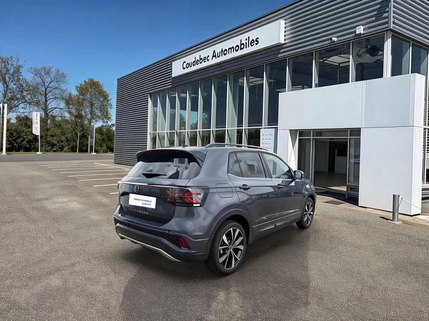 Volkswagen T-Cross gris en 3/4 arrière droit, avec jantes alliage et pare-chocs R-Line, devant un concessionnaire.
