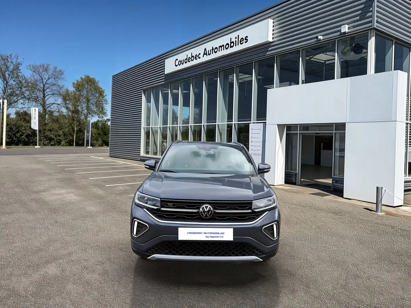 Volkswagen T-Cross gris vu de face devant un showroom avec calandre noire et feux LED allumés.