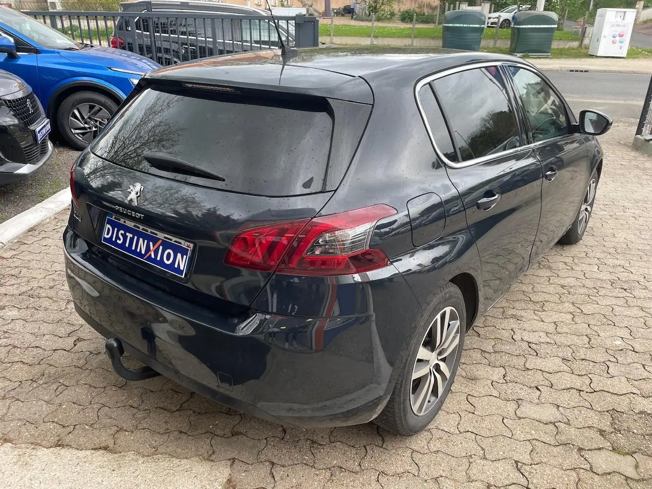 Vue 3/4 arrière droite d'une Peugeot 308 gris hurricane avec vitres arrière surteintées et feux arrière rouges.
