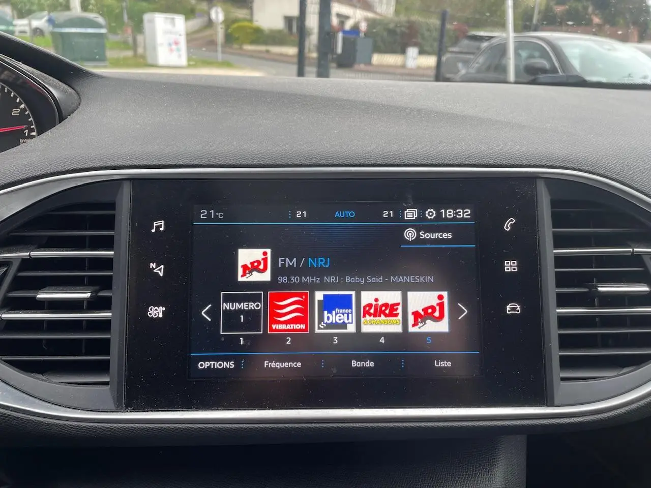Écran tactile central de la Peugeot 308 gris Hurricane affichant la radio FM NRJ avec commandes tactiles et aérateurs latéraux.