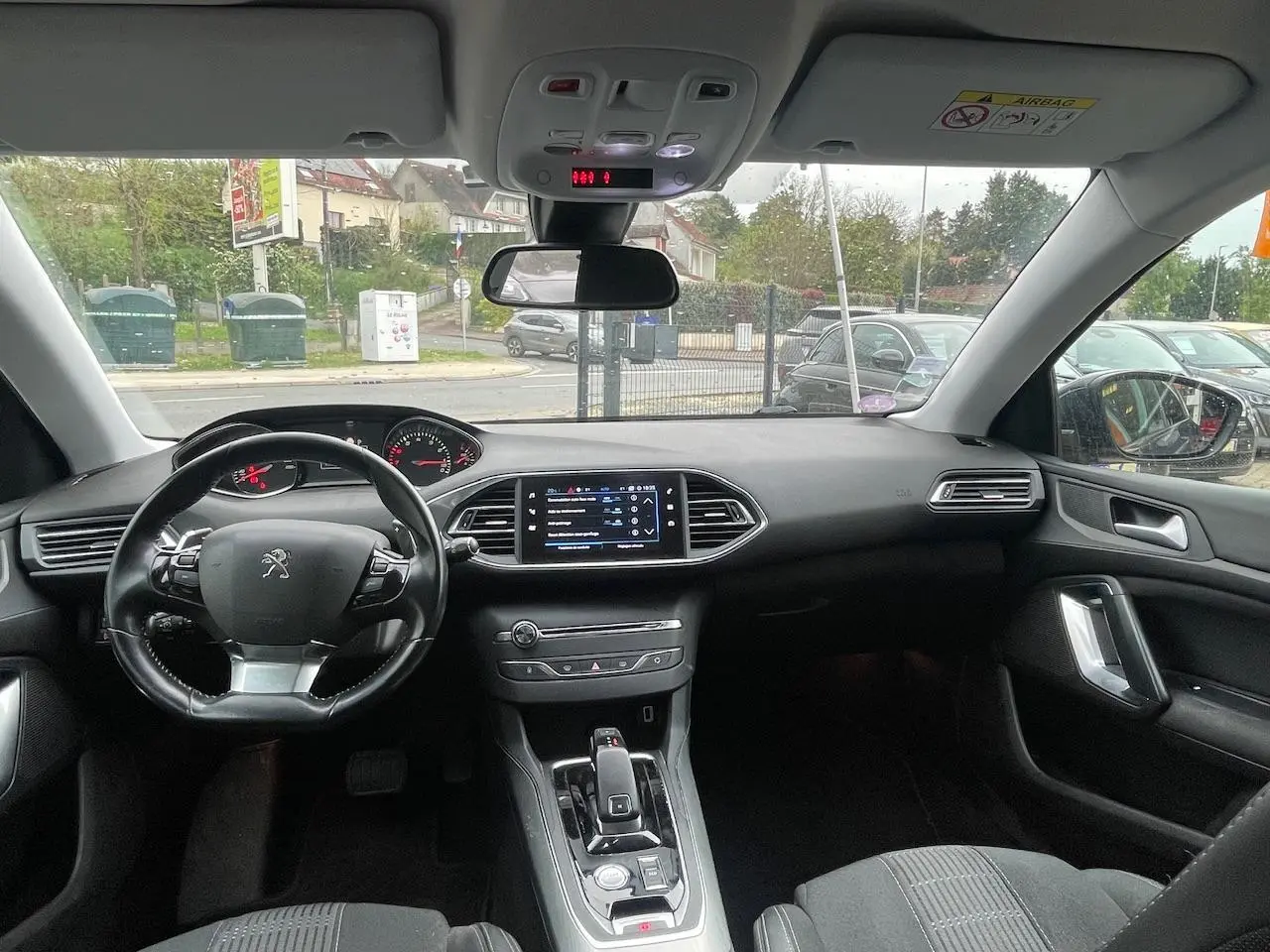 Vue intérieure avant de la Peugeot 308 gris Hurricane de 2018, montrant le tableau de bord, le volant multifonction et l'écran tactile central.