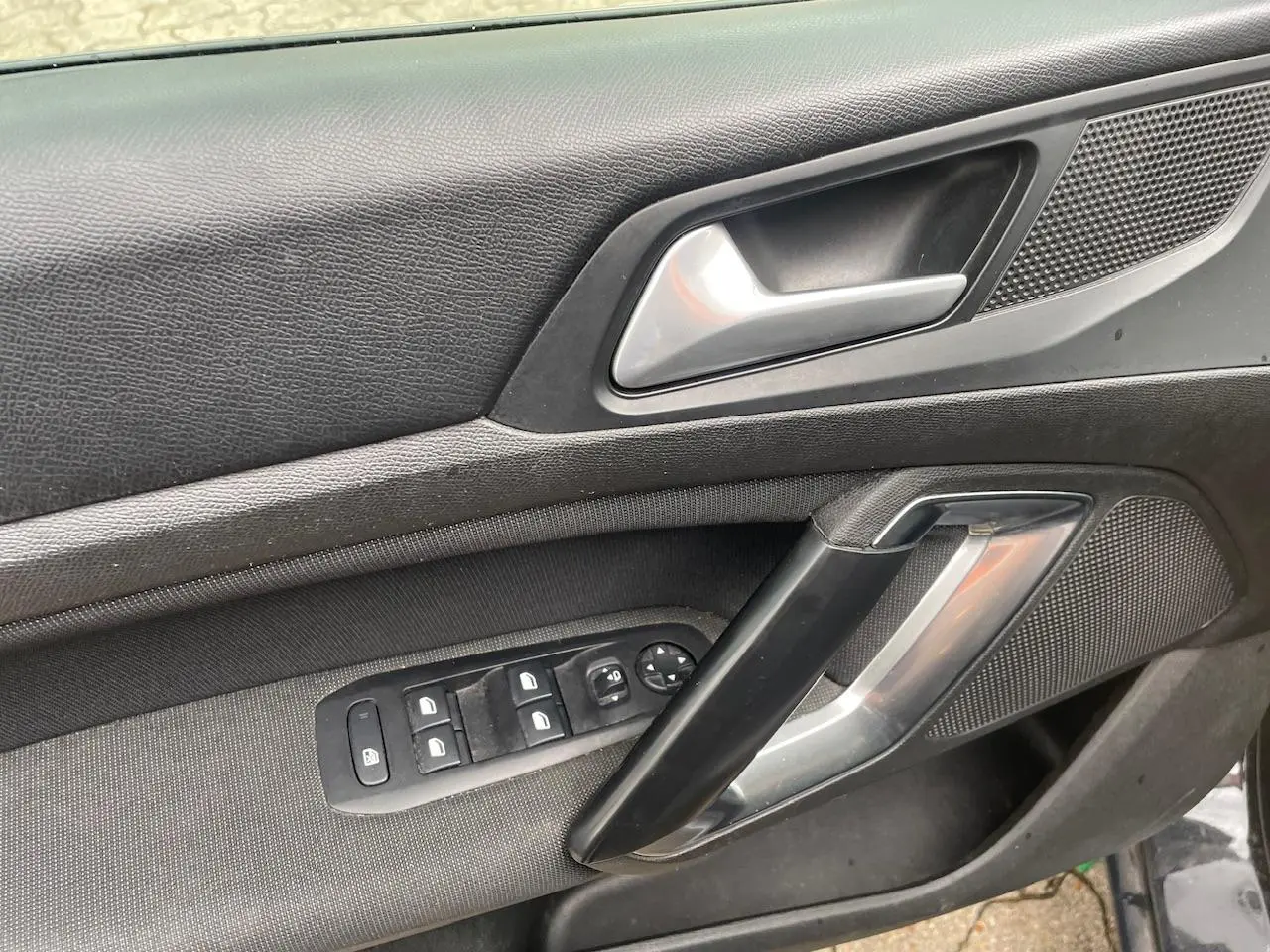 Intérieur côté gauche de la porte d’une Peugeot 308 gris Hurricane, avec commandes de vitres et poignée argentée.