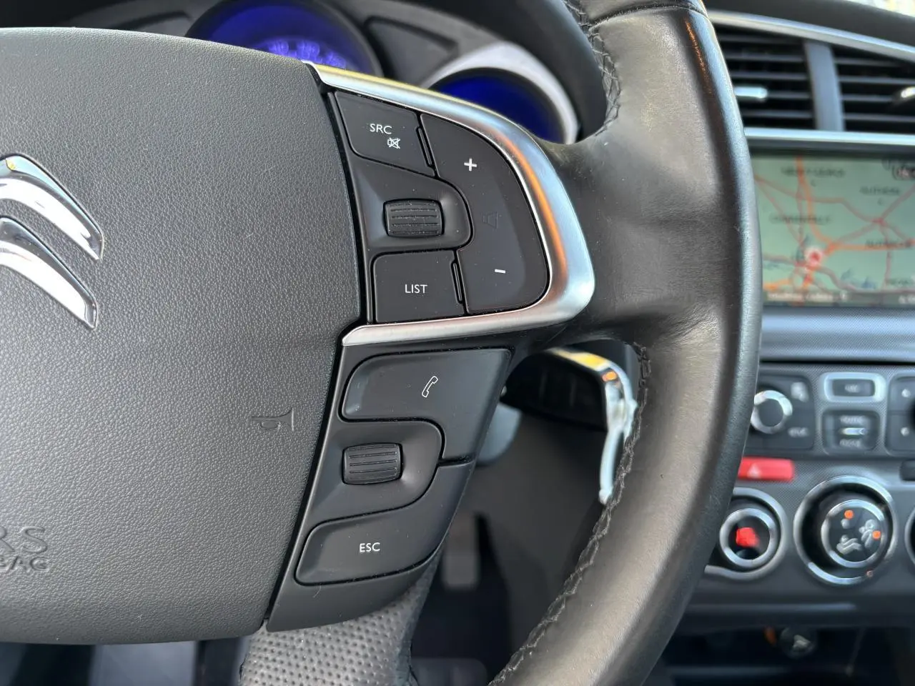 Gros plan sur le volant noir de la Citroën C4 2012 avec commandes intégrées et écran de navigation en arrière-plan.