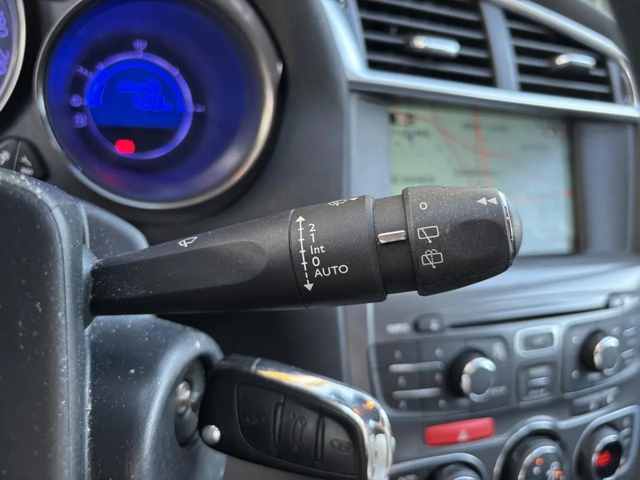 Gros plan sur la commande d'essuie-glace gauche du tableau de bord d'une Citroën C4 gris clair avec écran de navigation en arrière-plan.