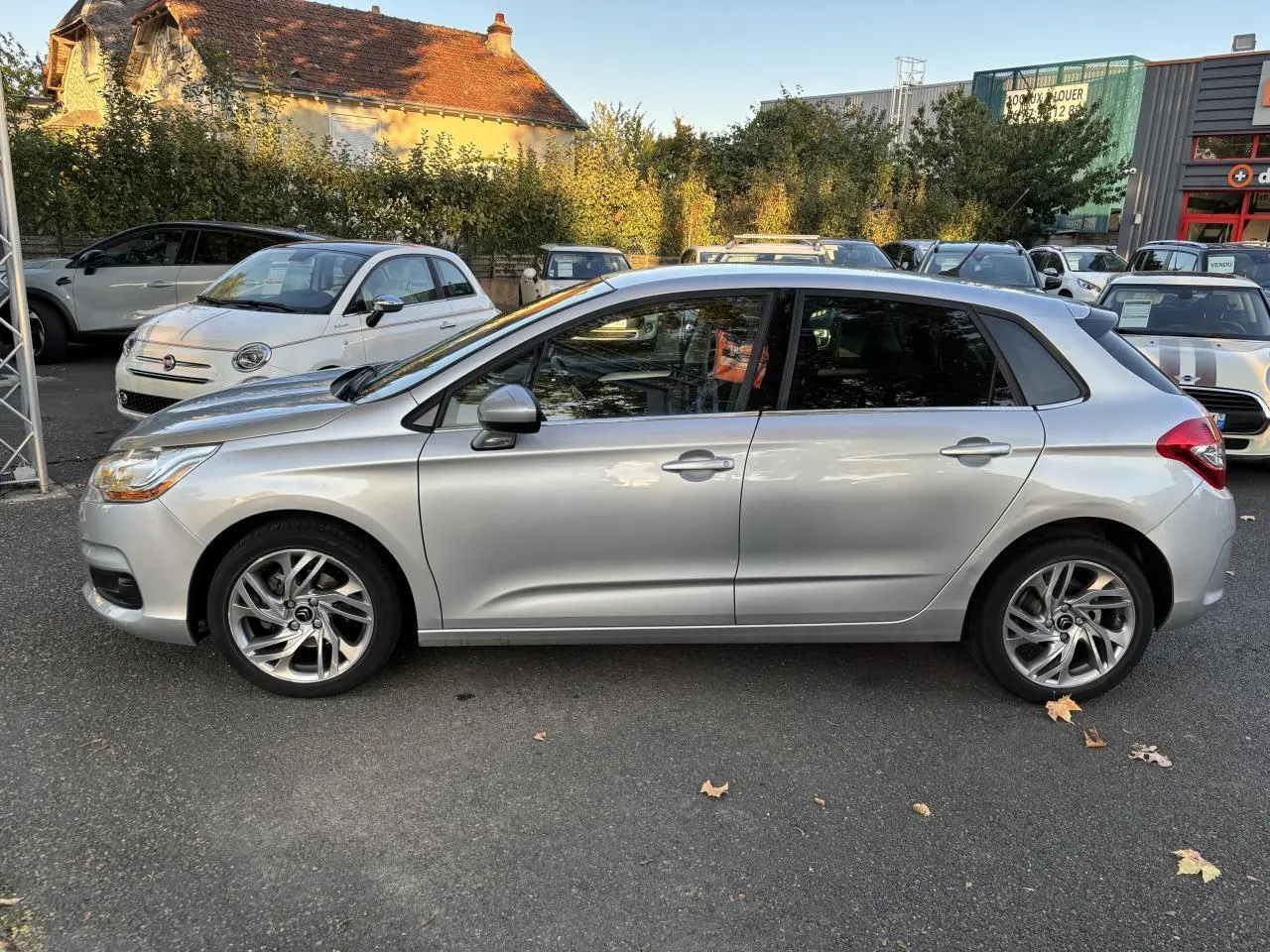 Profil côté gauche d'une Citroën C4 gris clair de 2012, avec vitres arrière surteintées et jantes alliage visibles.