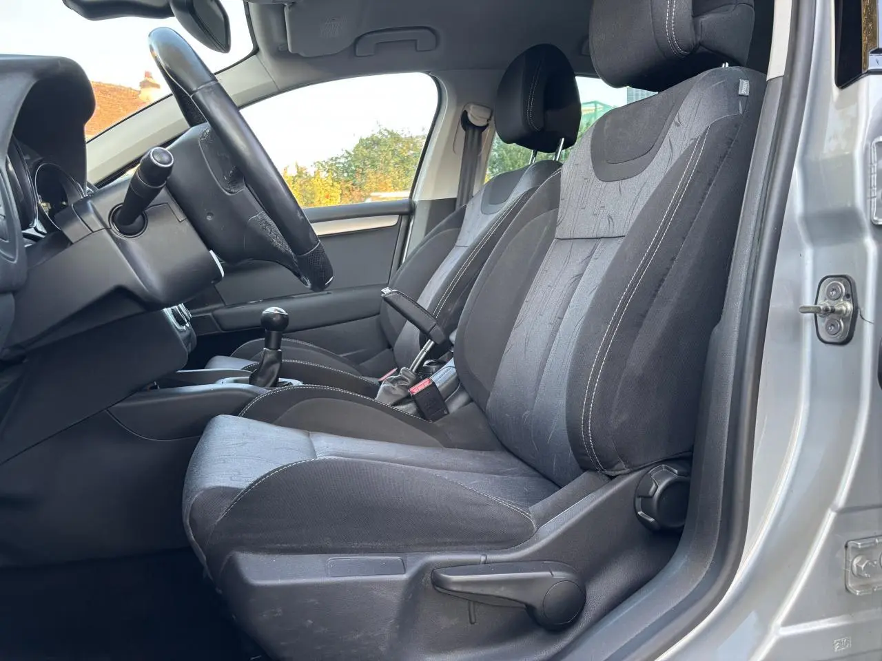 Vue intérieure côté conducteur de la Citroën C4 gris clair 2012, montrant sièges tissu noirs et levier de vitesse manuel.