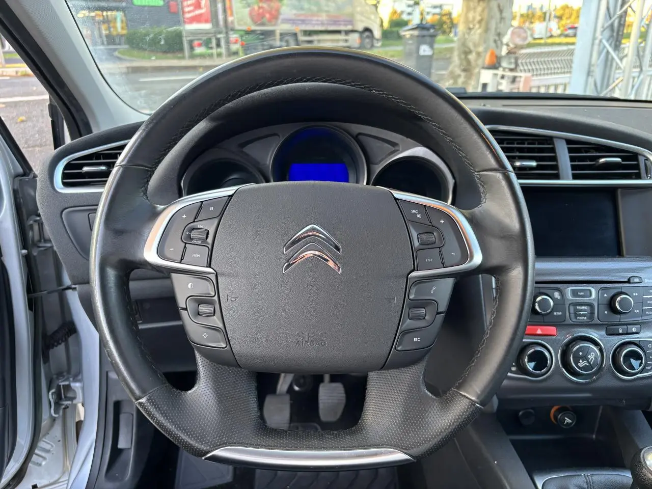 Vue intérieure centrée sur le volant multifonction noir de la Citroën C4 gris clair de 2012 avec tableau de bord visible.