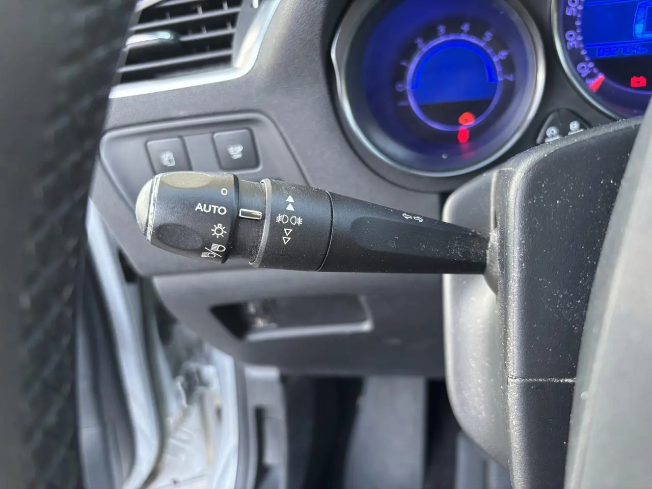 Gros plan sur la manette des phares et clignotants du tableau de bord d'une Citroën C4 gris clair de 2012.