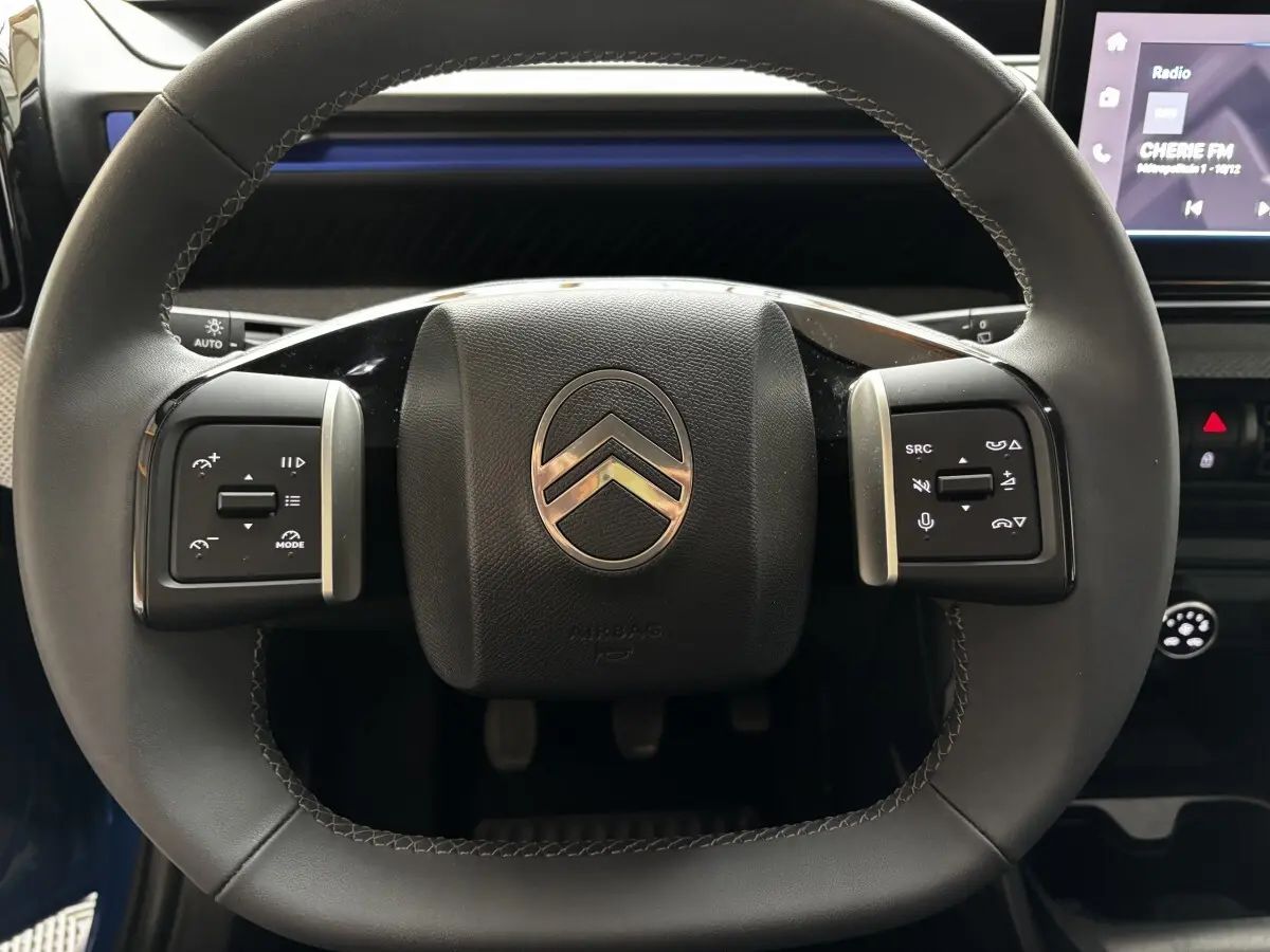 Gros plan sur le volant cuir noir de la Citroën C3 2025 avec commandes multifonctions et écran tactile en arrière-plan.