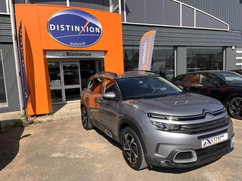 Vue 3/4 avant droite d'un Citroën C5 Aircross gris métallisé devant un concessionnaire avec jantes alliage distinctives.