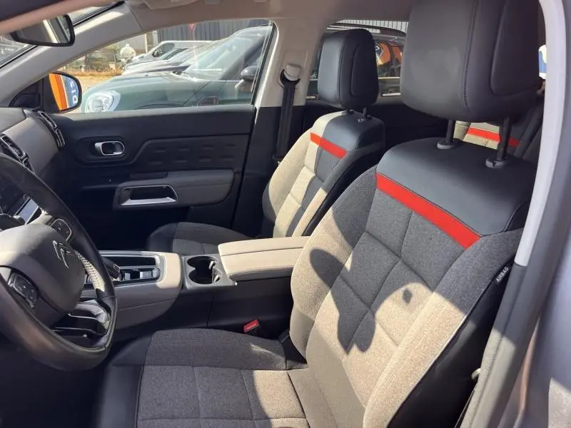 Vue intérieure côté conducteur de la Citroën C5 Aircross 2019, sièges tissu gris avec bande rouge et volant cuir noir.