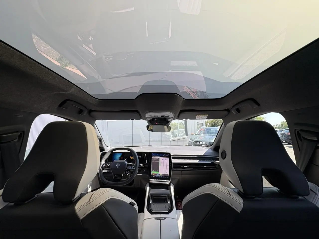Vue intérieure avant du Renault Espace 2025, sièges gris sable clair et toit panoramique en verre opacifiant.