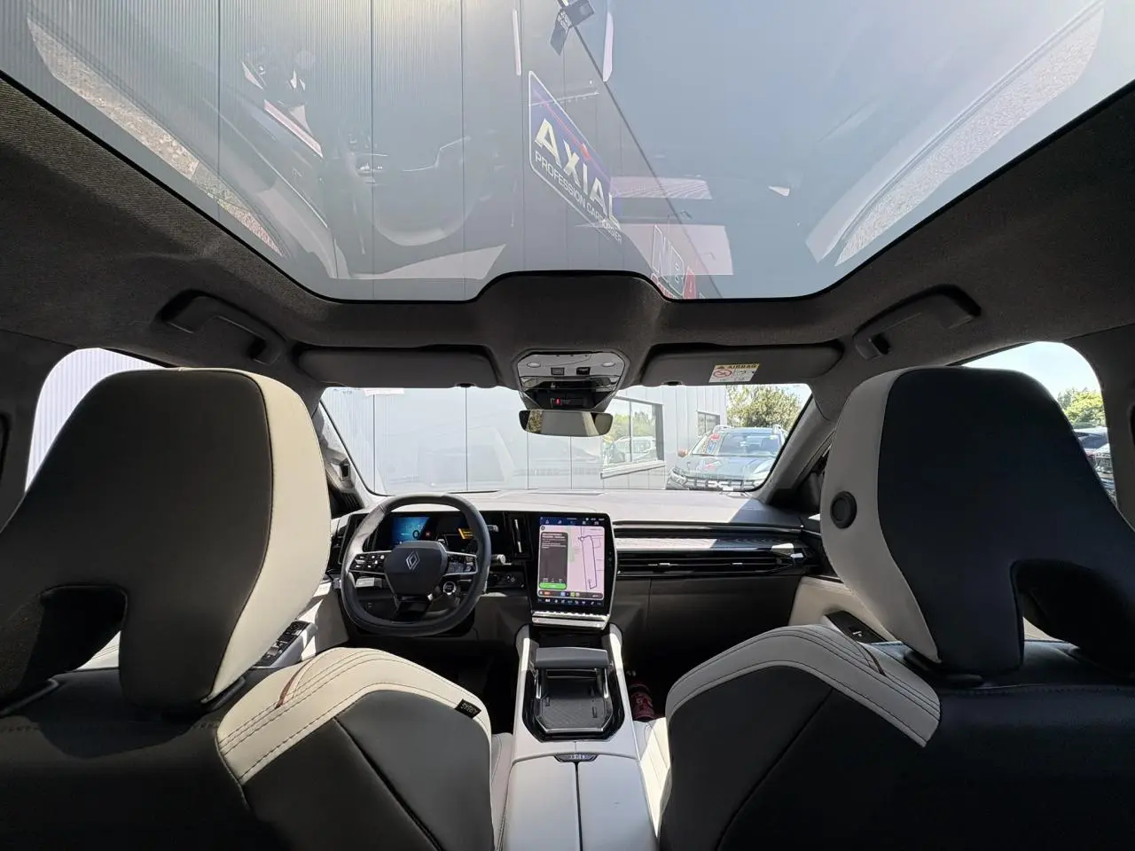 Vue intérieure avant du Renault Espace 2025 avec toit panoramique, sellerie gris sable clair et tableau de bord moderne.