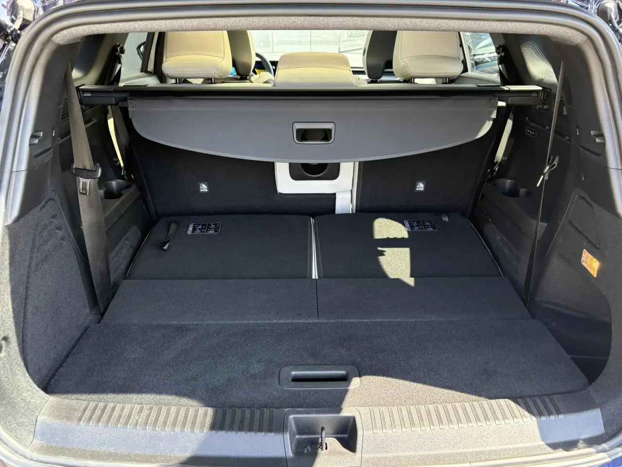 Vue arrière du coffre spacieux du Renault Espace VI hybride, banquette arrière rabattue et cache-bagages déployé.
