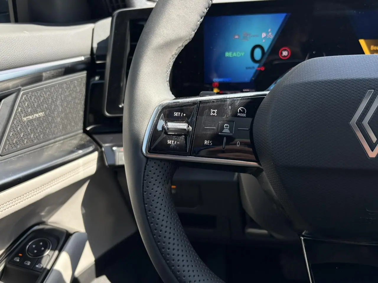 Gros plan sur le volant noir perforé et la planche de bord gris sable clair du Renault Espace VI hybride 2025.