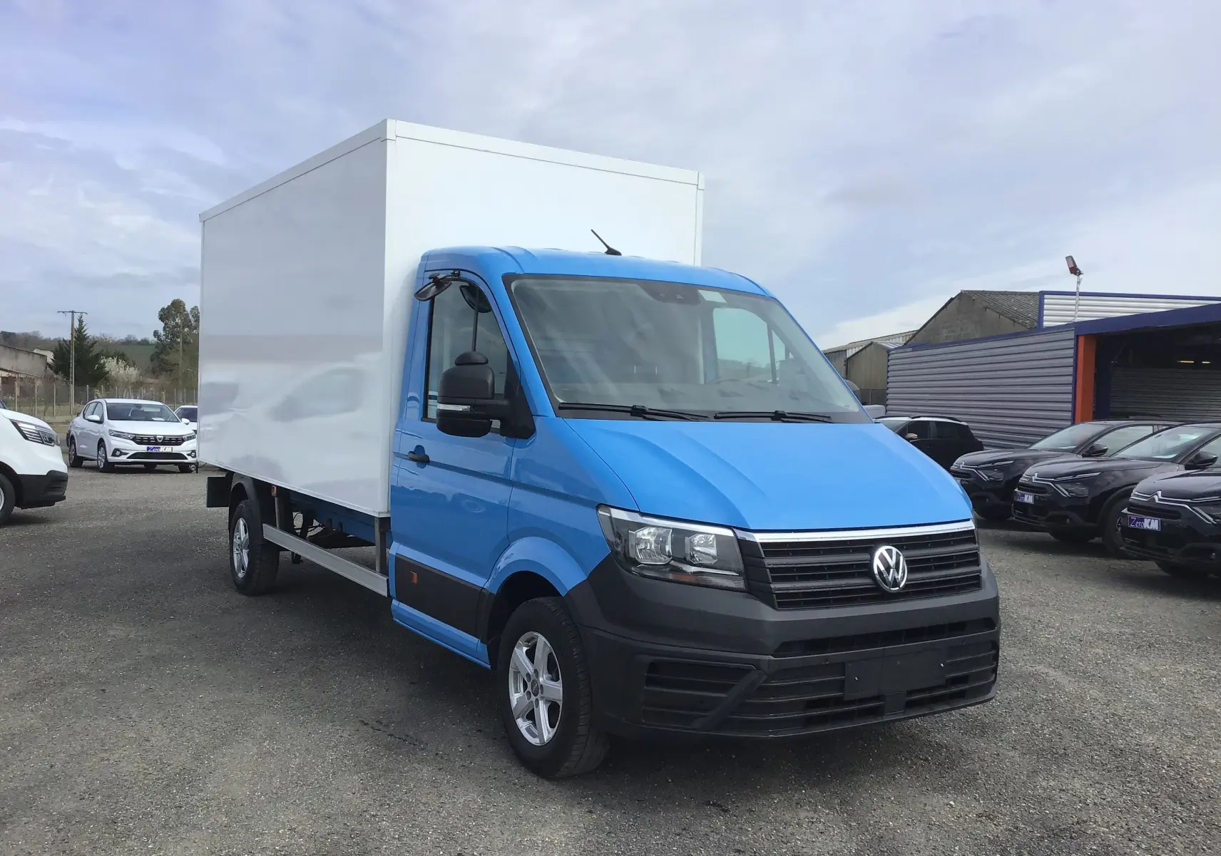 Volkswagen Crafter bleu en 3/4 avant droit avec caisse blanche et calandre noire sur parking extérieur.