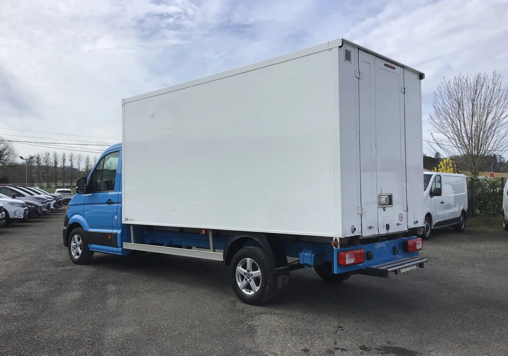 Vue 3/4 arrière droite du Volkswagen Crafter bleu avec caisse blanche, portes arrière fermées et jantes alliage 16 pouces.
