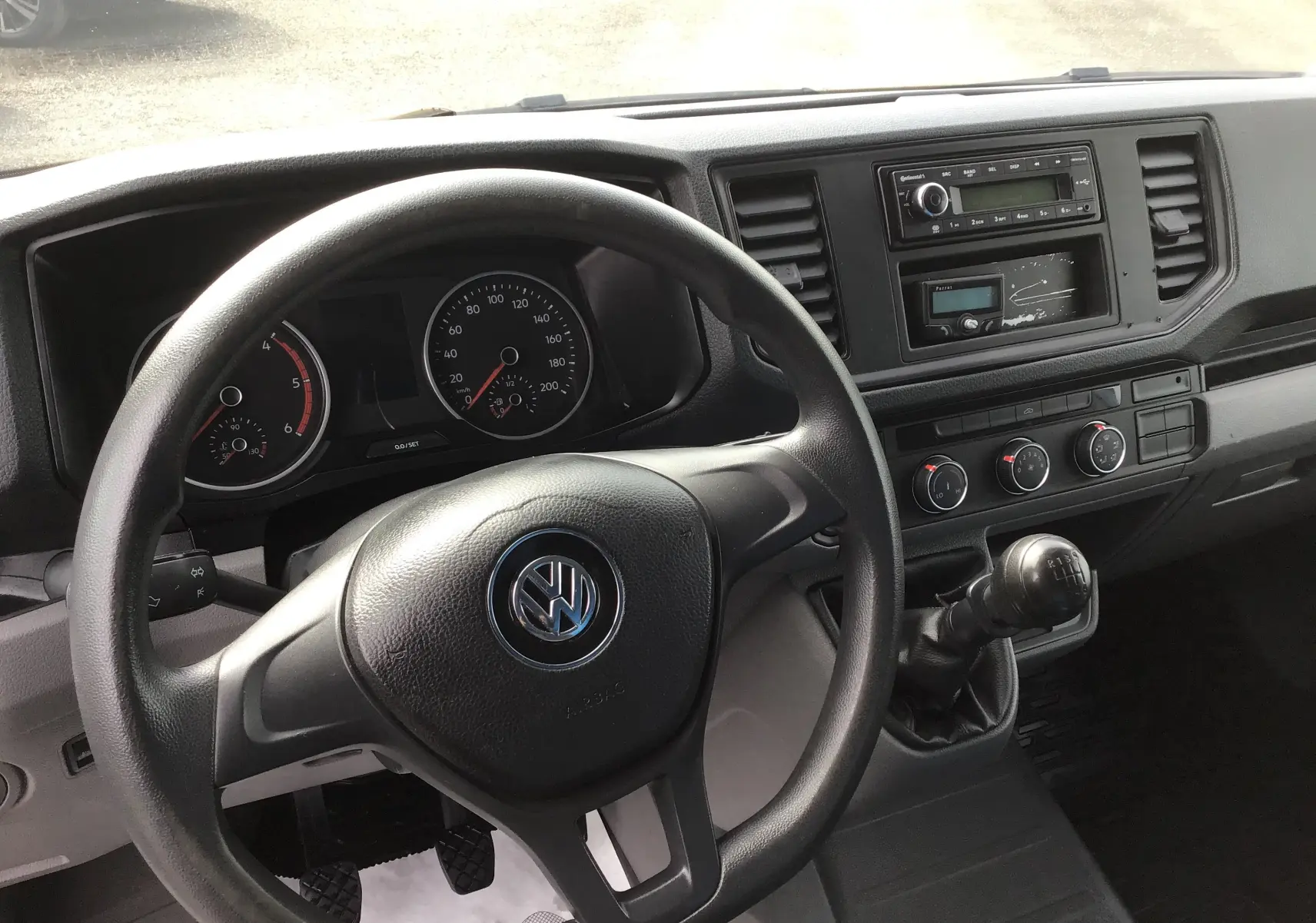 Vue intérieure du tableau de bord du Volkswagen Crafter bleu, avec volant, compteurs et levier de vitesses manuel visibles.