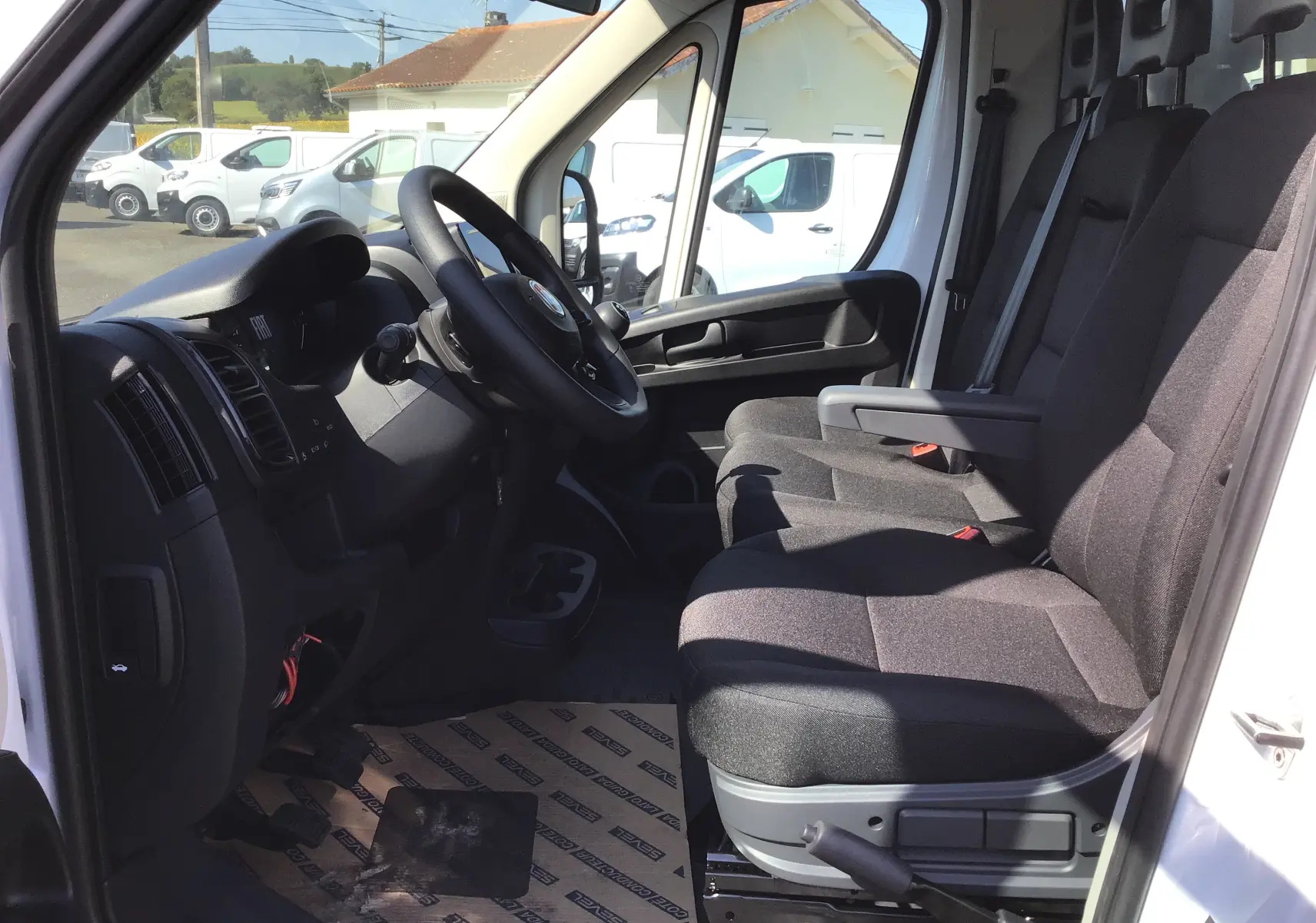 Intérieur côté conducteur du FIAT Ducato Chassis Benne blanc 2023, montrant sièges tissu noir et tableau de bord simple.