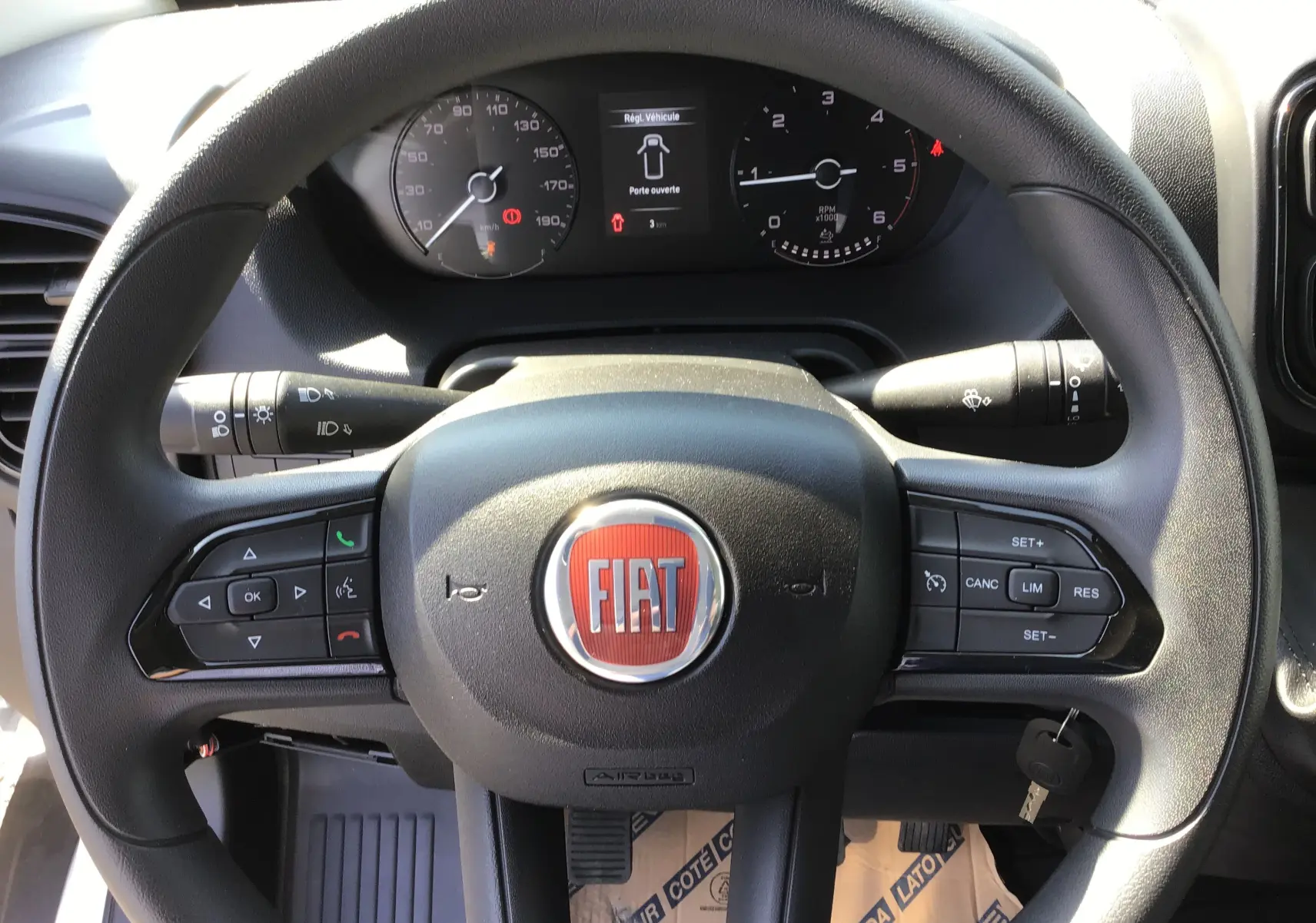 Vue rapprochée du volant FIAT du Ducato Chassis Benne 2023 avec commandes intégrées et tableau de bord numérique.