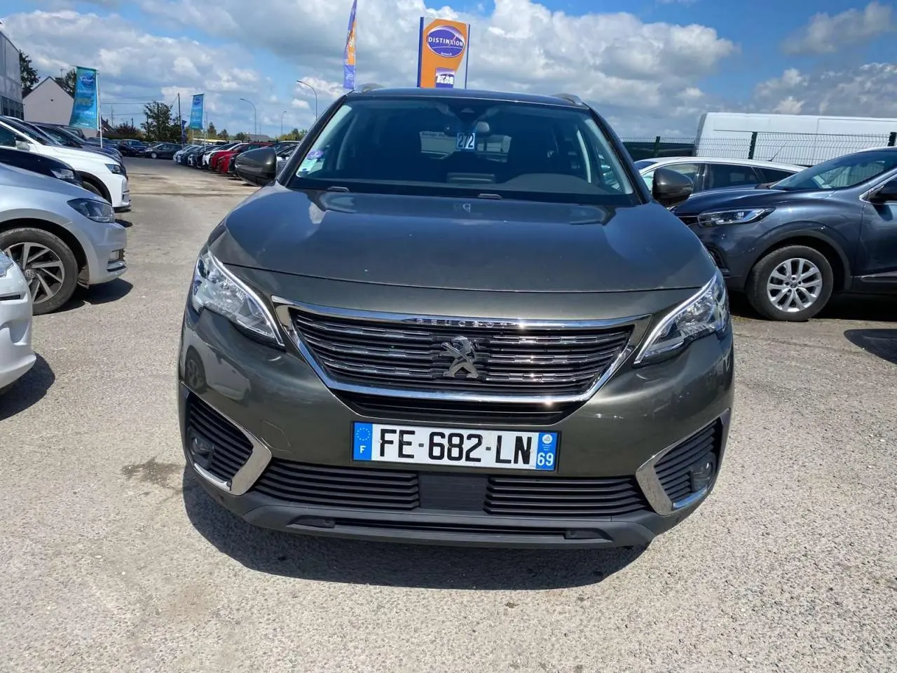 Vue avant d'un Peugeot 5008 gris clair garé en extérieur, avec calandre chromée et plaque d'immatriculation française visible.